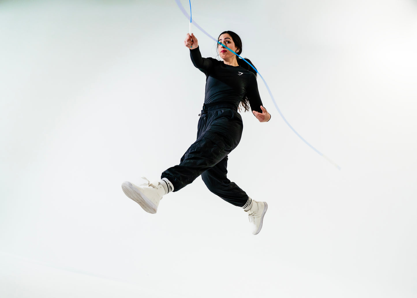 Person in black outfit with white shoes holding a blue rope against a white background