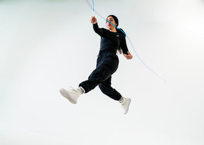 Person in black outfit with white shoes holding a blue rope against a white background